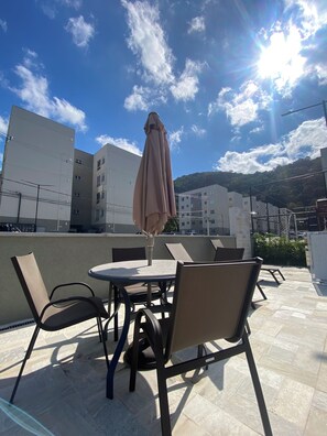Eine Dachterrasse mit Tisch und Stühlen, einem Sonnenschirm und Blick auf Gebäude und Hügel.