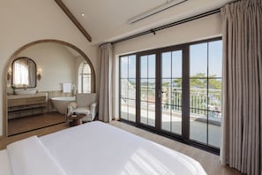 Quarto de hotel com uma cama grande, banheiro com banheira, toucador e varanda com vista.