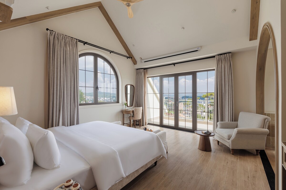Quarto de hotel com uma cama grande, uma escrivaninha, uma cadeira e vista para a cidade.