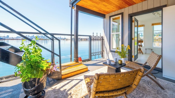 A balcony with a view of the water, a wooden chair, a table, and a potted plant.
