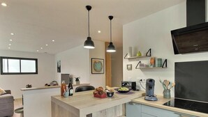 Een moderne keuken met een centraal eiland, hanglampen, een flatscreen televisie en een koffieapparaat.