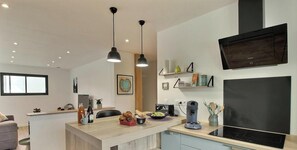 A modern kitchen with a central island, pendant lights, a flat-screen TV, and a coffee machine. - Ker Alran - PLENEUF VAL ANDRE (PLENEUF VAL ANDRE)