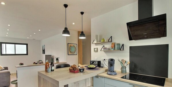 A modern kitchen with a central island, pendant lights, a flat-screen TV, and a coffee machine. - Ker Alran - PLENEUF VAL ANDRE (PLENEUF VAL ANDRE)