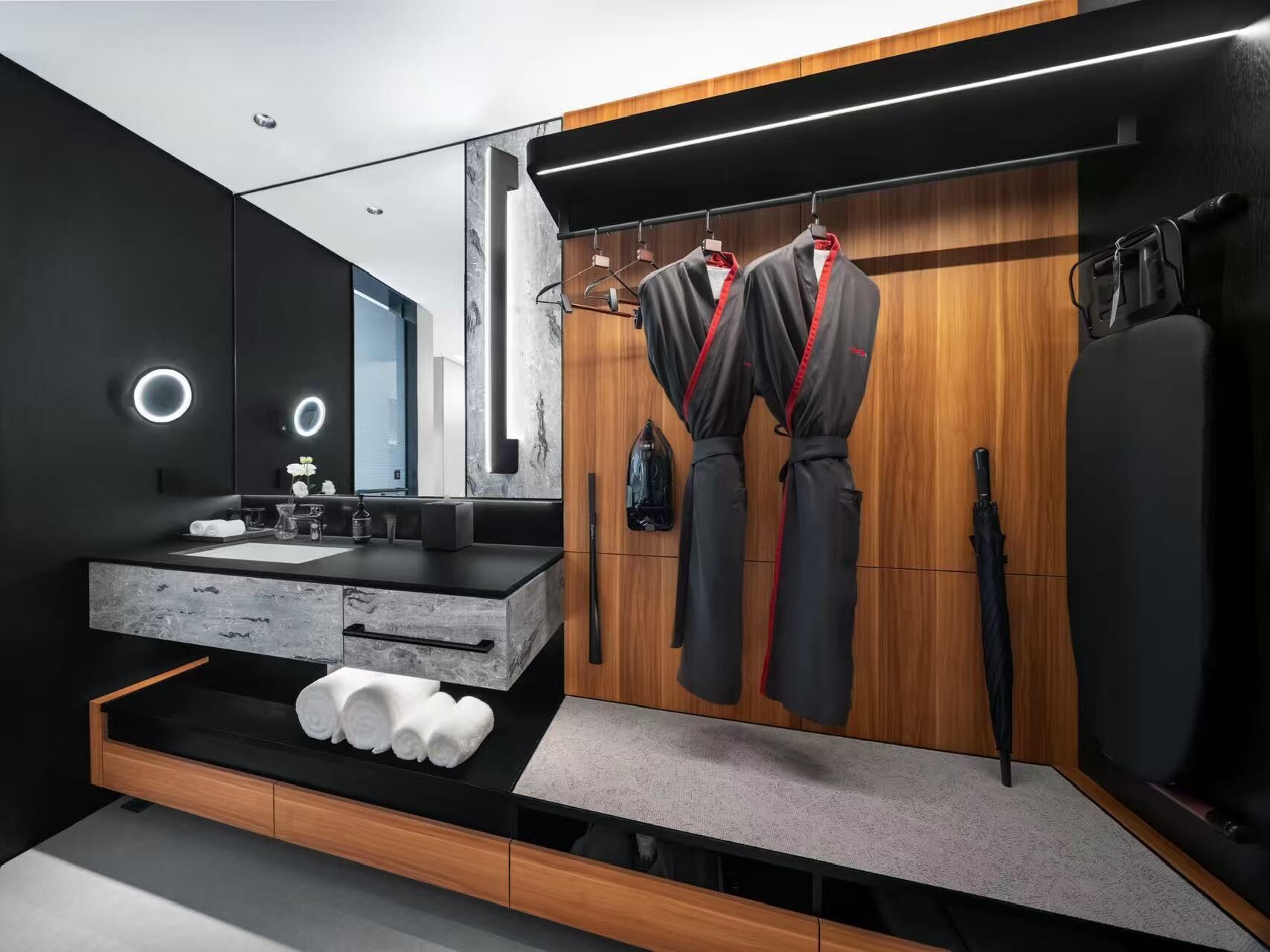 Une salle de bain moderne avec un grand miroir, un meuble-lavabo en bois et un porte-serviettes avec des peignoirs.