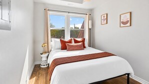 A bedroom with a bed, a window, a bedside table, and two framed pictures on the wall. - Walkerville 1BR | Parking + WiFi + Workspace (Windsor)