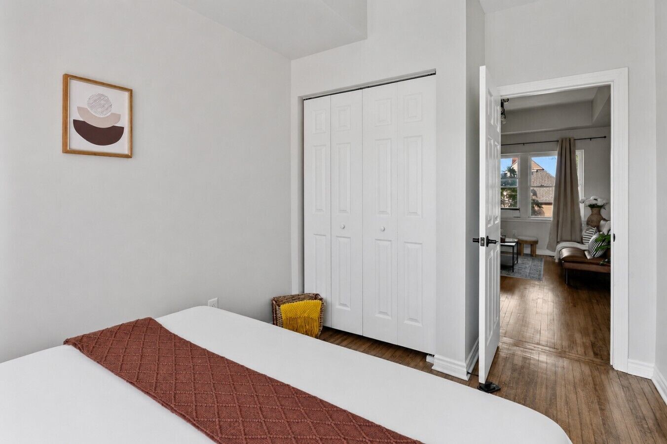 Quarto com cama, porta branca e vista para outro cômodo com mesa e cadeira.