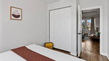 Quarto com cama, porta branca e vista para outro cômodo com mesa e cadeira.