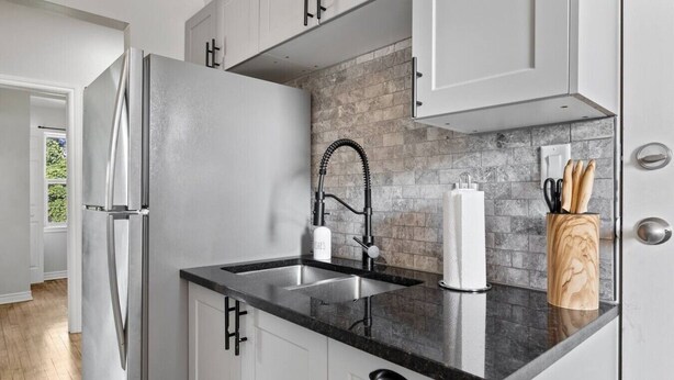 A kitchen with a stainless steel refrigerator, a double sink, and a backsplash of gray tiles. - Walkerville 1BR | Parking + WiFi + Workspace (Windsor)