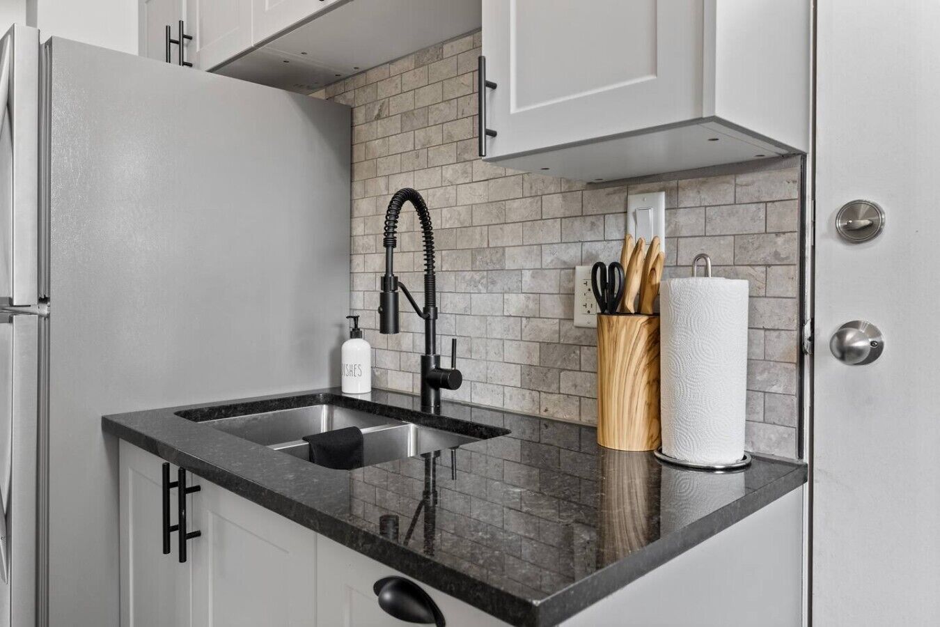 Una cocina con encimera negra, pileta de acero inoxidable y grifo moderno.