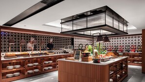 A modern kitchen with wooden cabinetry, a central island, and a chef preparing food. - IntercityHotel Taikoo Li Chunxi Rd (Chengdu)
