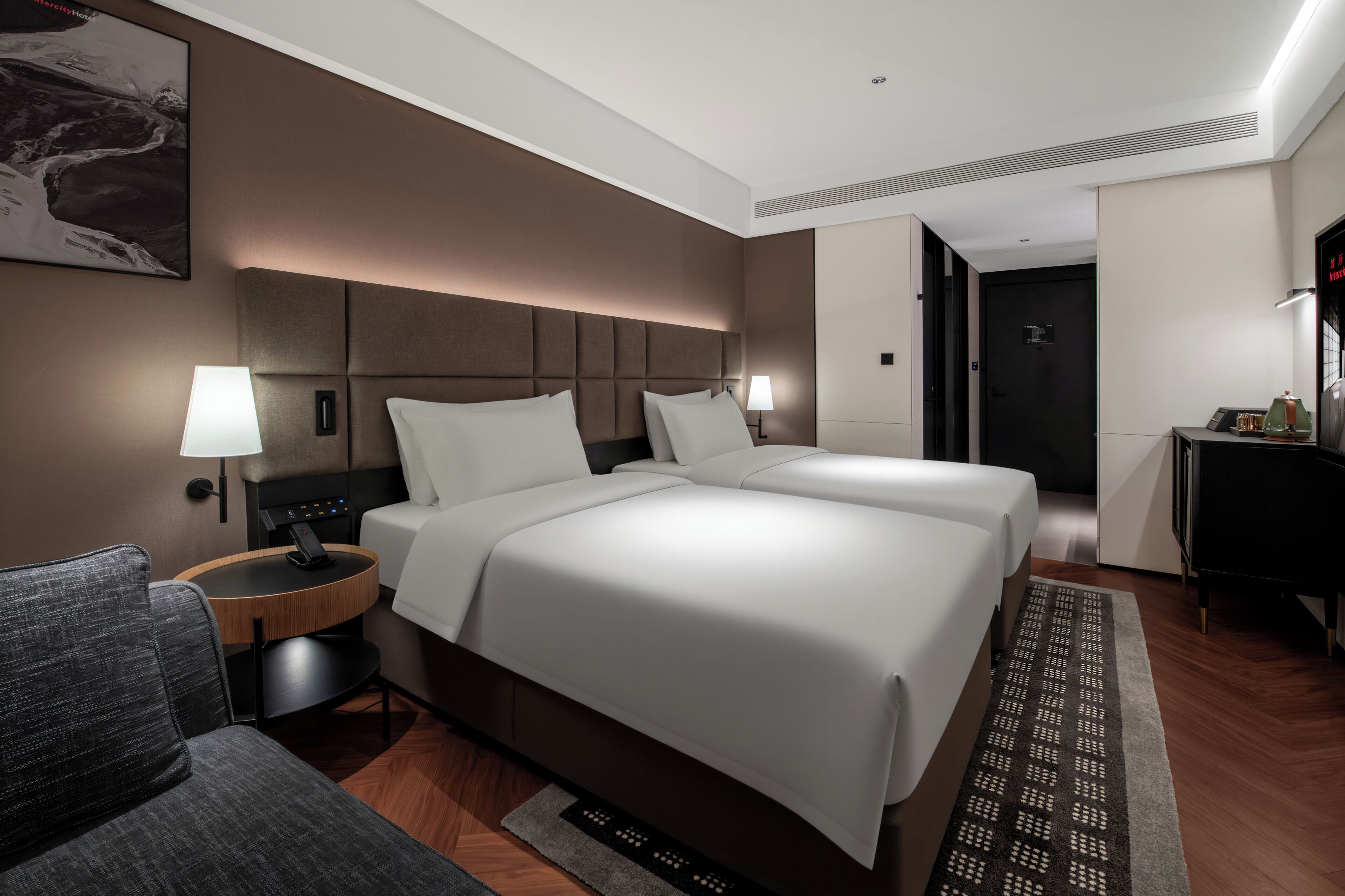 Une chambre d’hôtel avec un grand lit, deux tables de chevet avec des lampes, un canapé et une vue sur le couloir.