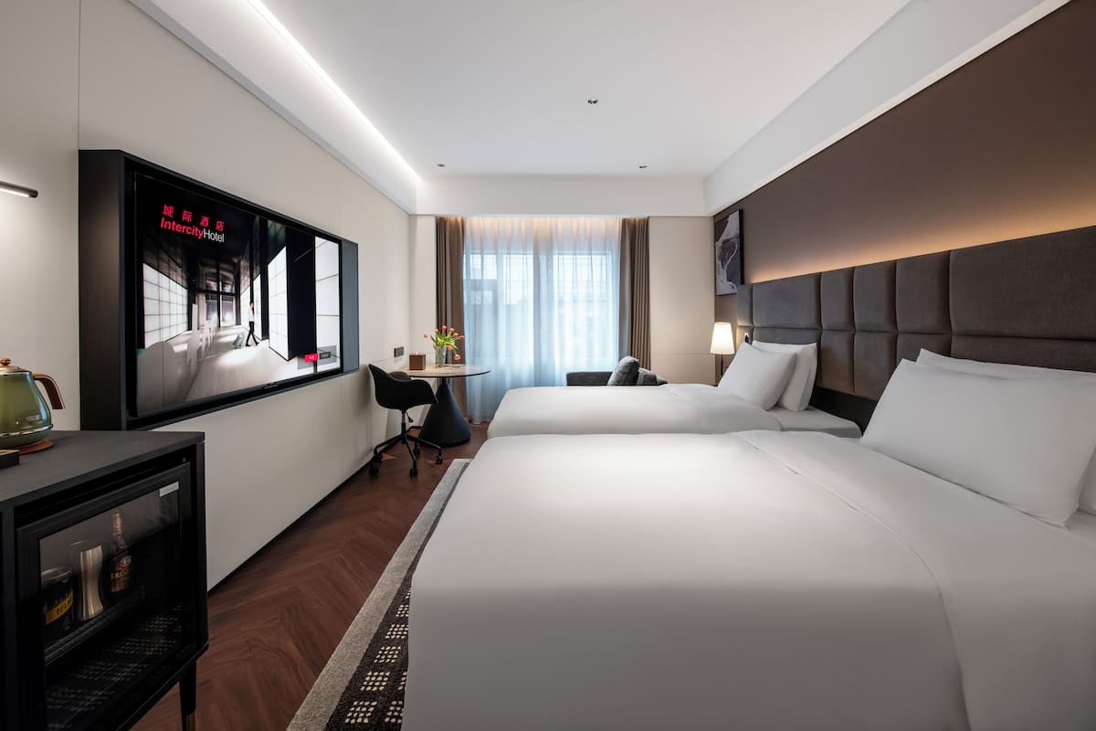 A hotel room with a large bed, a desk, a chair, a television, and a window with curtains.
