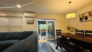 A living room with a sofa, a dining table with chairs, a sliding glass door leading to a patio, and a ceiling fan.