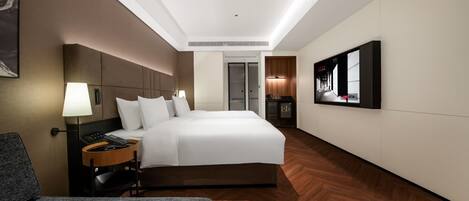 A modern hotel room with a large bed, bedside table, lamp, and a television on the wall.