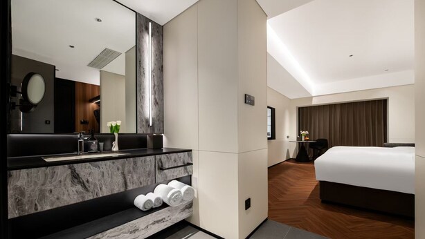 Quarto de hotel moderno com toucador de mármore, cama grande e área de estar separada.
