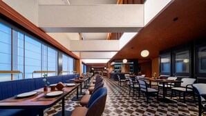 Um restaurante moderno com mesas compridas, assentos estofados azuis e chão estampado.