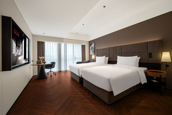 A hotel room with a large bed, a desk, a chair, and a large window with curtains.