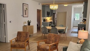 A spacious living area with a green sofa, two wooden armchairs, a round coffee table, and a patterned rug.