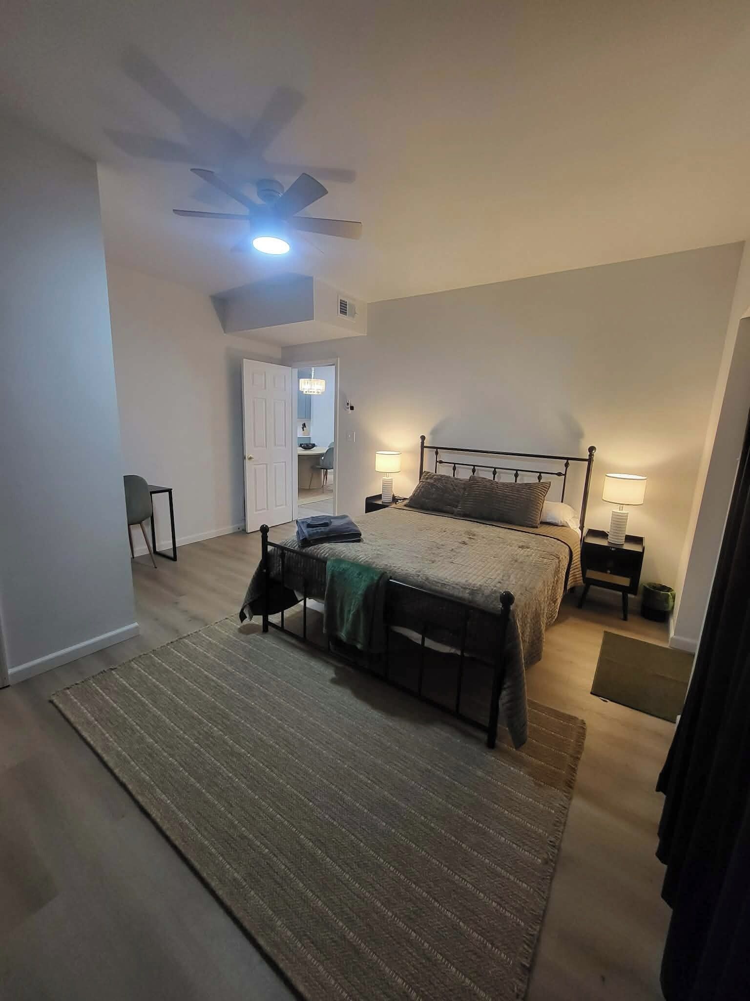 Una camera da letto con un letto, comodini, una ventola a soffitto e una porta che dà su un'altra stanza.
