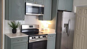 A kitchen with teal cabinets, a stainless steel refrigerator, a microwave, and a stove.