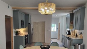 A modern kitchen with grey cabinets, a round dining table with chairs, and a hanging light fixture.
