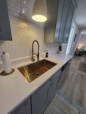 Una cocina moderna con encimera blanca, pileta de acero inoxidable y armarios grises.
