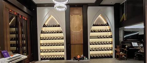 A modern interior with a central wooden door, two symmetrical wine racks on either side, a chandelier, and a piano.