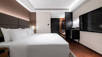 A modern hotel room with a large bed, a TV, a wardrobe, and a desk.