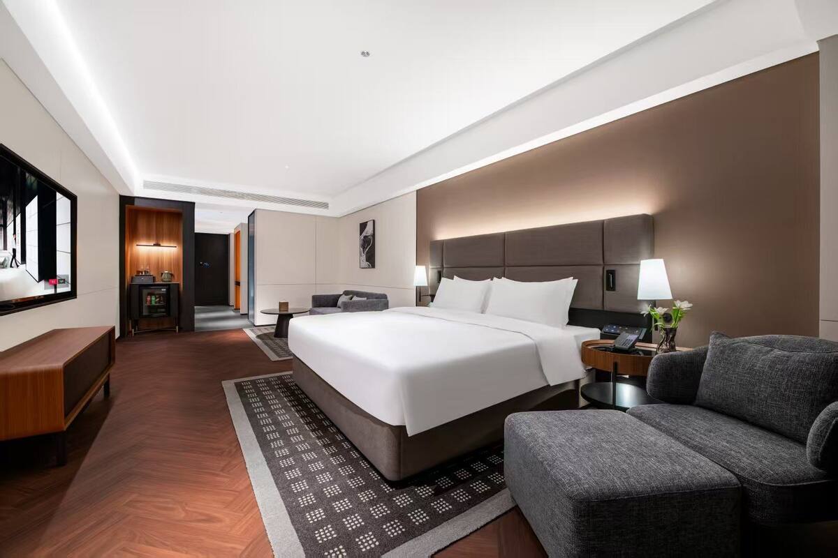 Una habitación de hotel moderna con una cama grande, una zona de estar, un escritorio y un televisor.