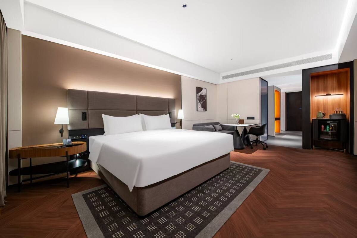Una habitación de hotel con una cama grande, un escritorio, una silla, una mesita y un refrigerador.
