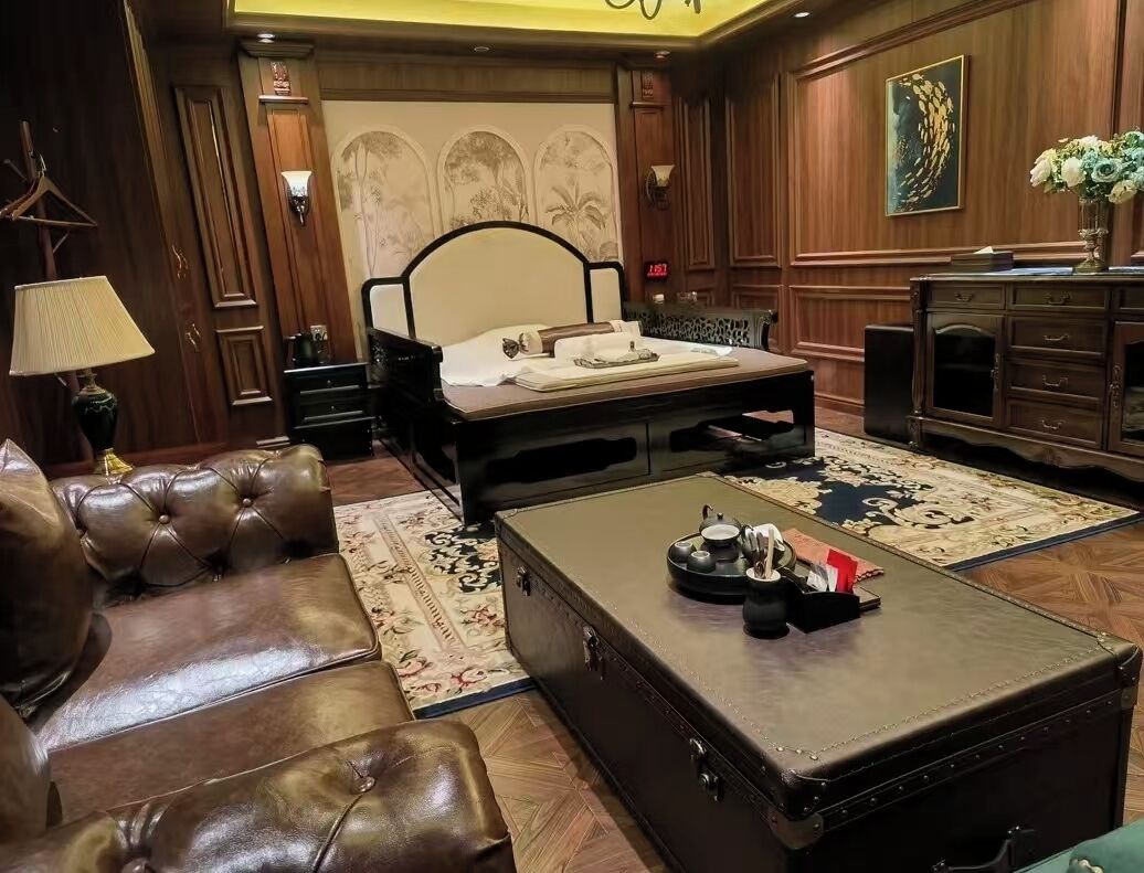 A hotel room with a bed, a leather sofa, a wooden dresser, and a vintage suitcase on the floor.