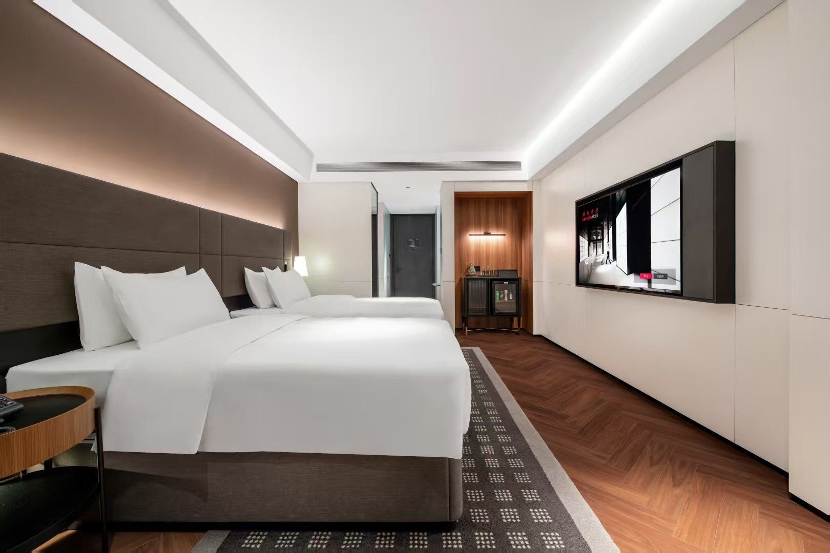A hotel room with a large bed, a TV mounted on the wall, and a small cabinet.