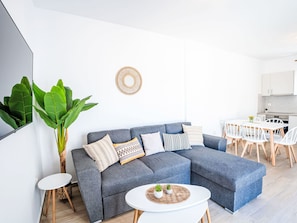 Ein modernes Wohnzimmer mit einer grauen Eckcouch, einem runden Couchtisch und einem Essbereich mit einem weißen Tisch und Stühlen.