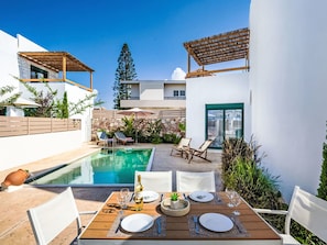 Ein moderner Essbereich im Freien mit Pool, weißen Wänden und einer Pergola.