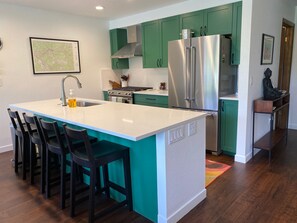 Una cocina con una isla central, armarios verdes, un refrigerador de acero inoxidable y un mapa en la pared.