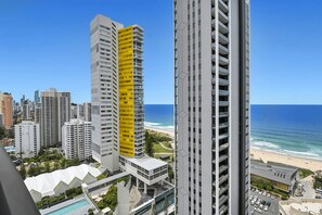 Ein Hochhaus mit auffälligem, gelbem Abschnitt, mit Blick auf einen Strand unter blauem Himmel.