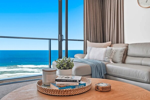 Ein Zimmer mit Meerblick, eine Couch, ein Couchtisch mit Büchern und einer Kerze sowie ein Blumentopf.