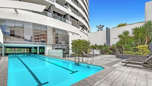 A modern building with a swimming pool, outdoor seating, and a clear sky. - Sandy Beach Views at Oracle Level 25 (Gold Coast)