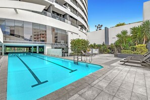 Ein modernes Gebäude mit Swimmingpool, Sitzgelegenheiten im Freien und blauem Himmel.