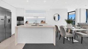 A modern kitchen with a central island, stainless steel appliances, and a dining area with a round table and chairs. - Sandy Beach Views at Oracle Level 25 (Gold Coast)