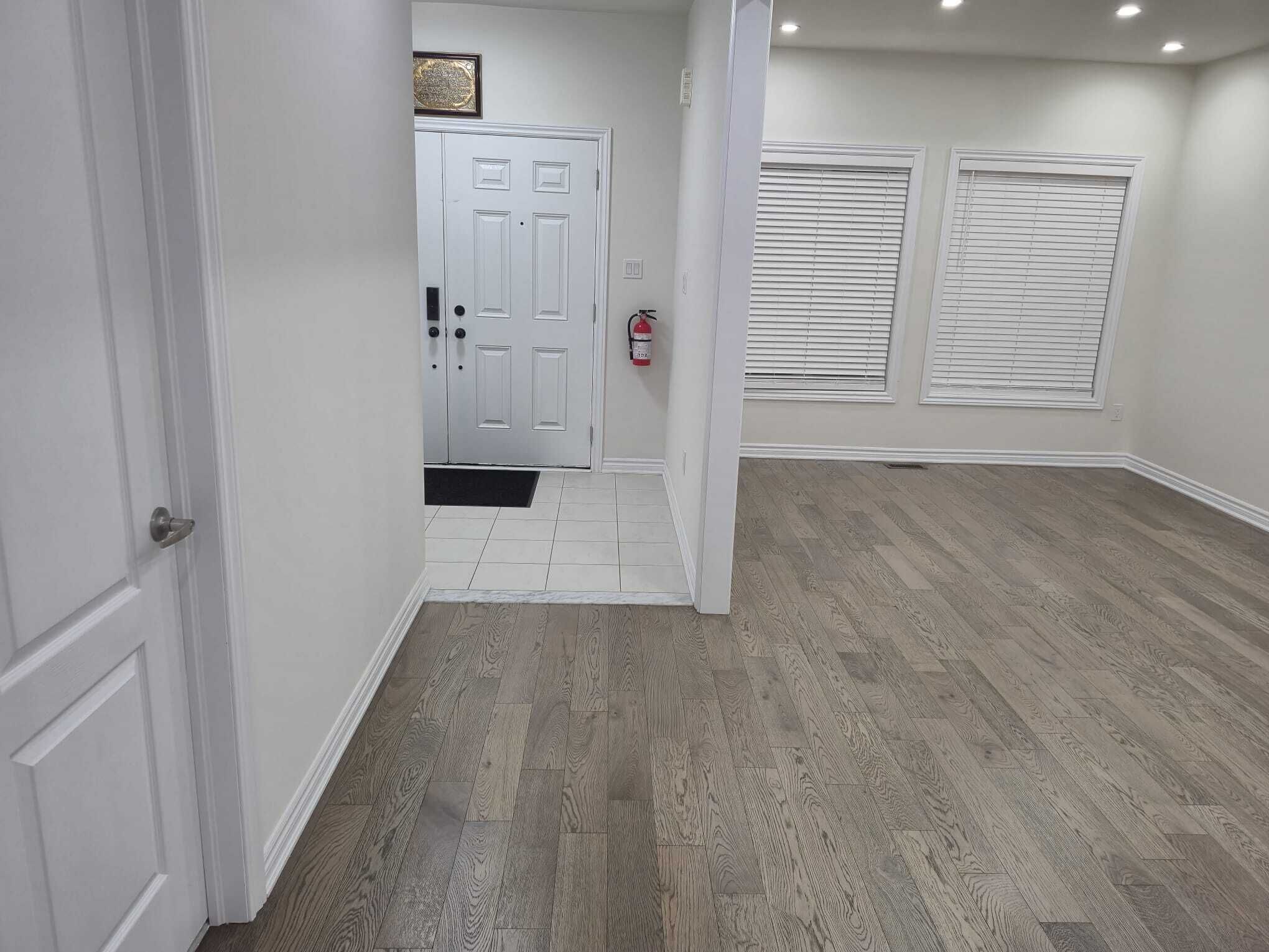 A hallway with a white door, a fire extinguisher, and a window with blinds.