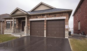 Une maison d’habitation avec une façade en briques, deux portes de garage et un porche à l’avant.