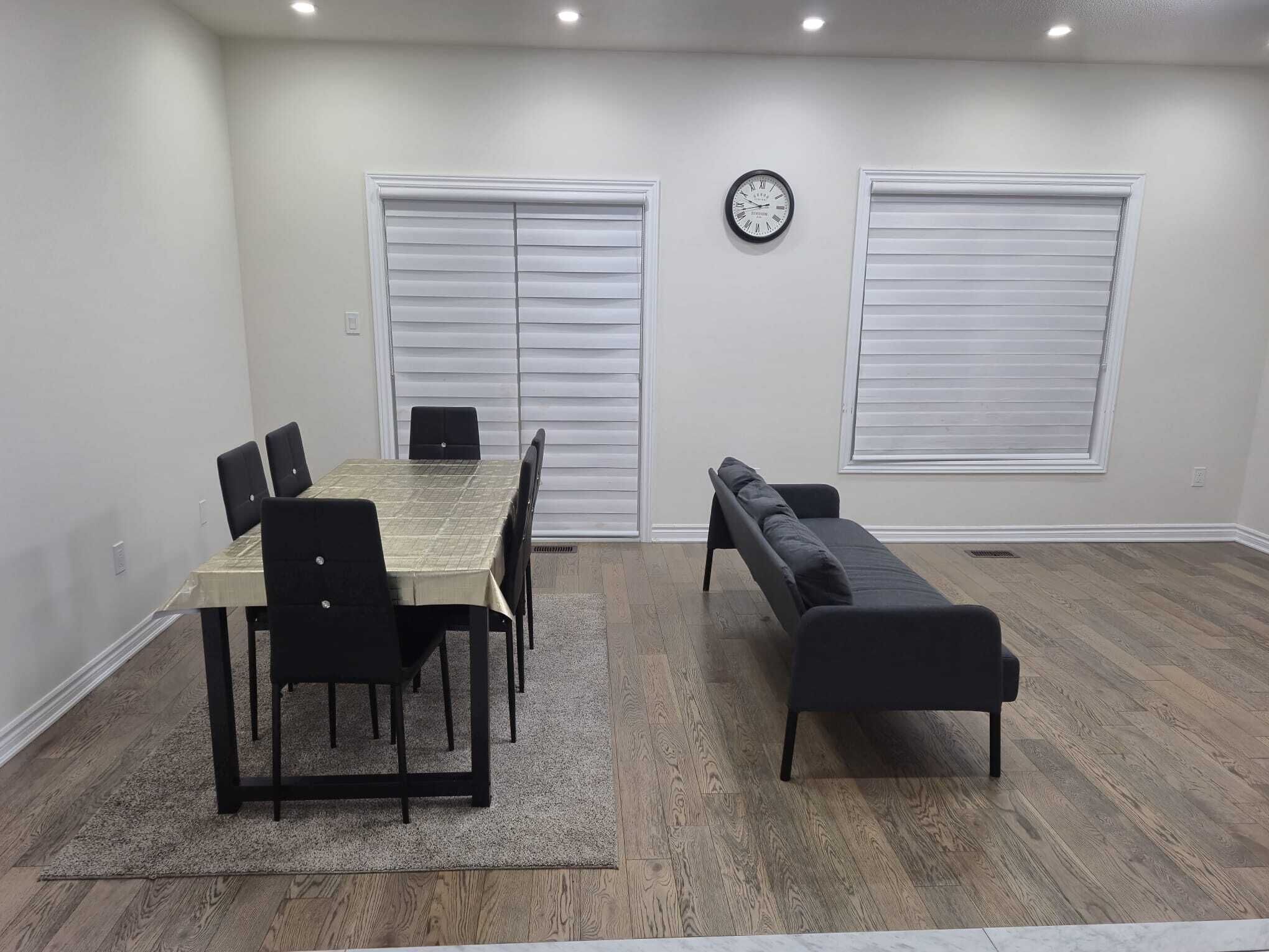 Una habitación con una mesa de comedor, sillas, un sofá y dos ventanas con persianas.