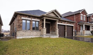 Une maison à deux étages, construite en briques, avec un porche à l’avant, deux portes de garage et une pelouse bien entretenue.
