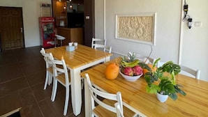 Un comedor con una mesa de madera y sillas blancas, un frutero y una planta en maceta.