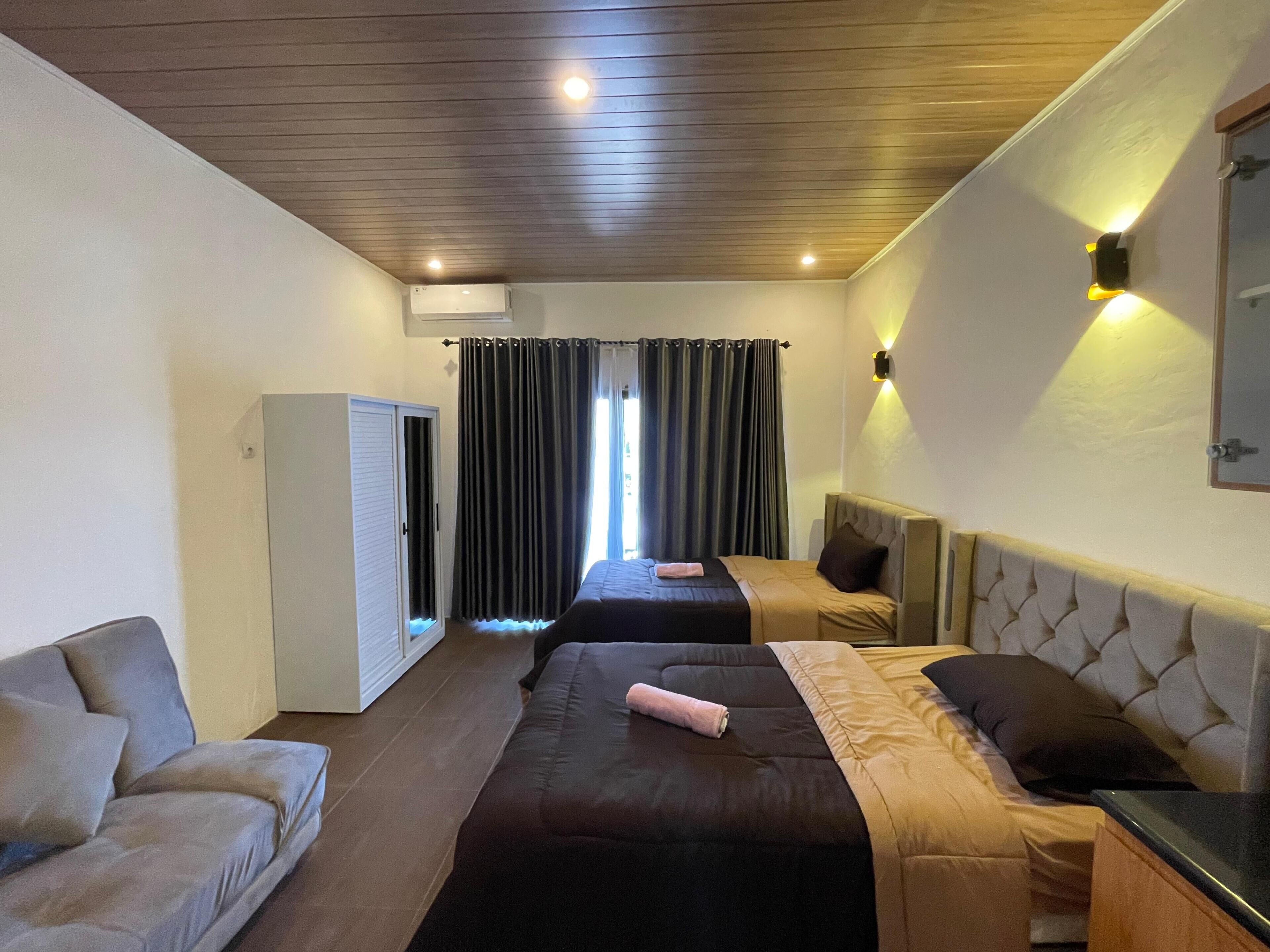 A hotel room with two beds, a sofa, a wardrobe, and a mirror on the wall.