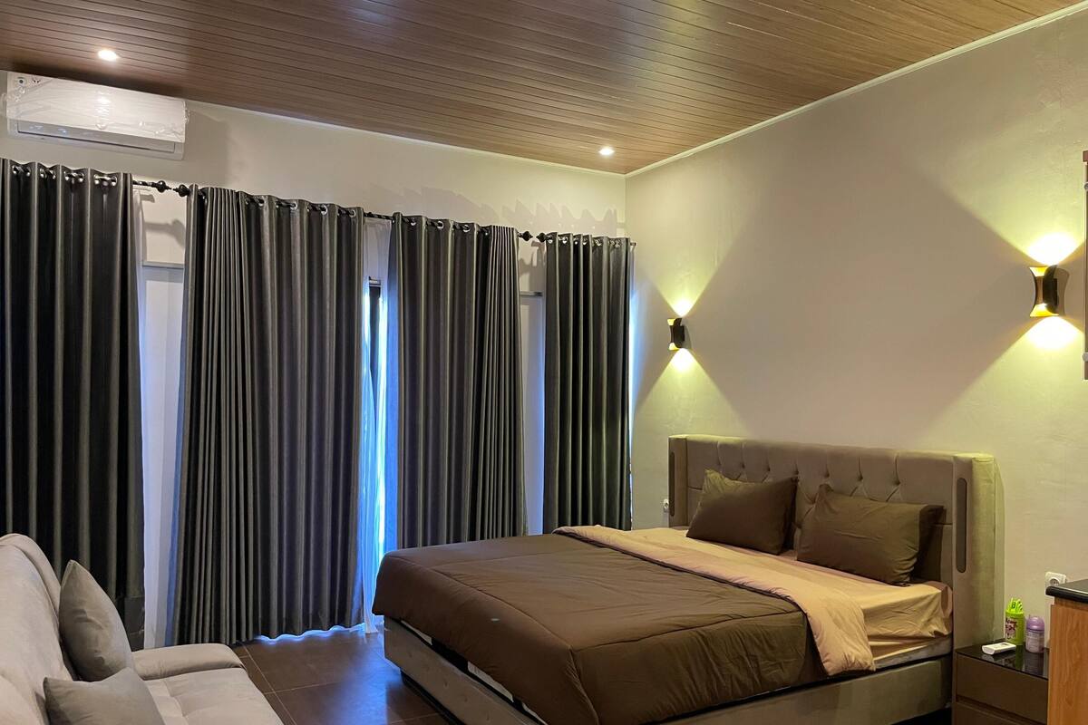 Una habitación de hotel con una cama, un sofá, una lámpara fijada en la pared y un equipo de aire acondicionado.