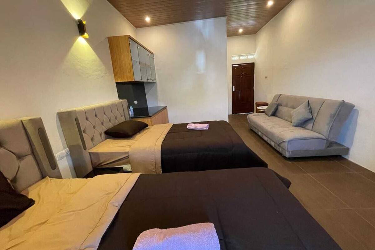 Habitación de hotel con dos camas, un sofá, una kitchenette y una puerta que da a otra habitación.