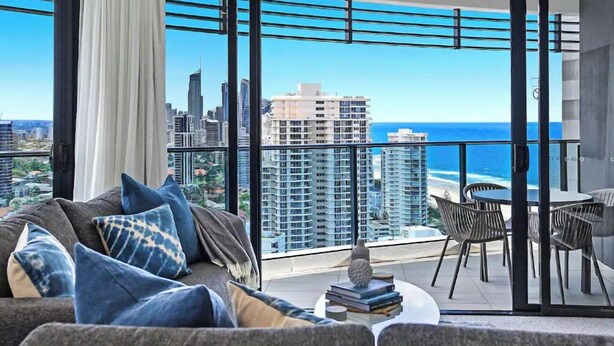 A balcony with a city view, a sofa with cushions, and a table with books. - Best Beach Views at Oracle Level 27 (Gold Coast City)