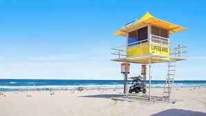 A lifeguard tower with a yellow roof and a sign, located on a beach with the ocean in the background. - Best Beach Views at Oracle Level 27 (Gold Coast City)
